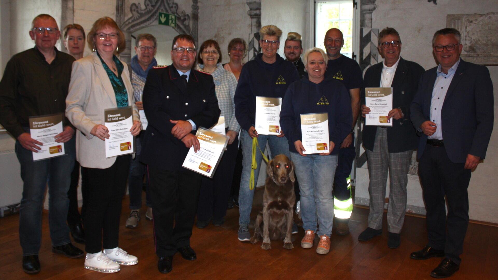 Gruppenfoto von geehrten Ehrenamtlichen mit Urkunden in den Händen. In der Mitte ein Feuerwehrmann in Uniform, im Vordergrund ein Hund an der Leine.