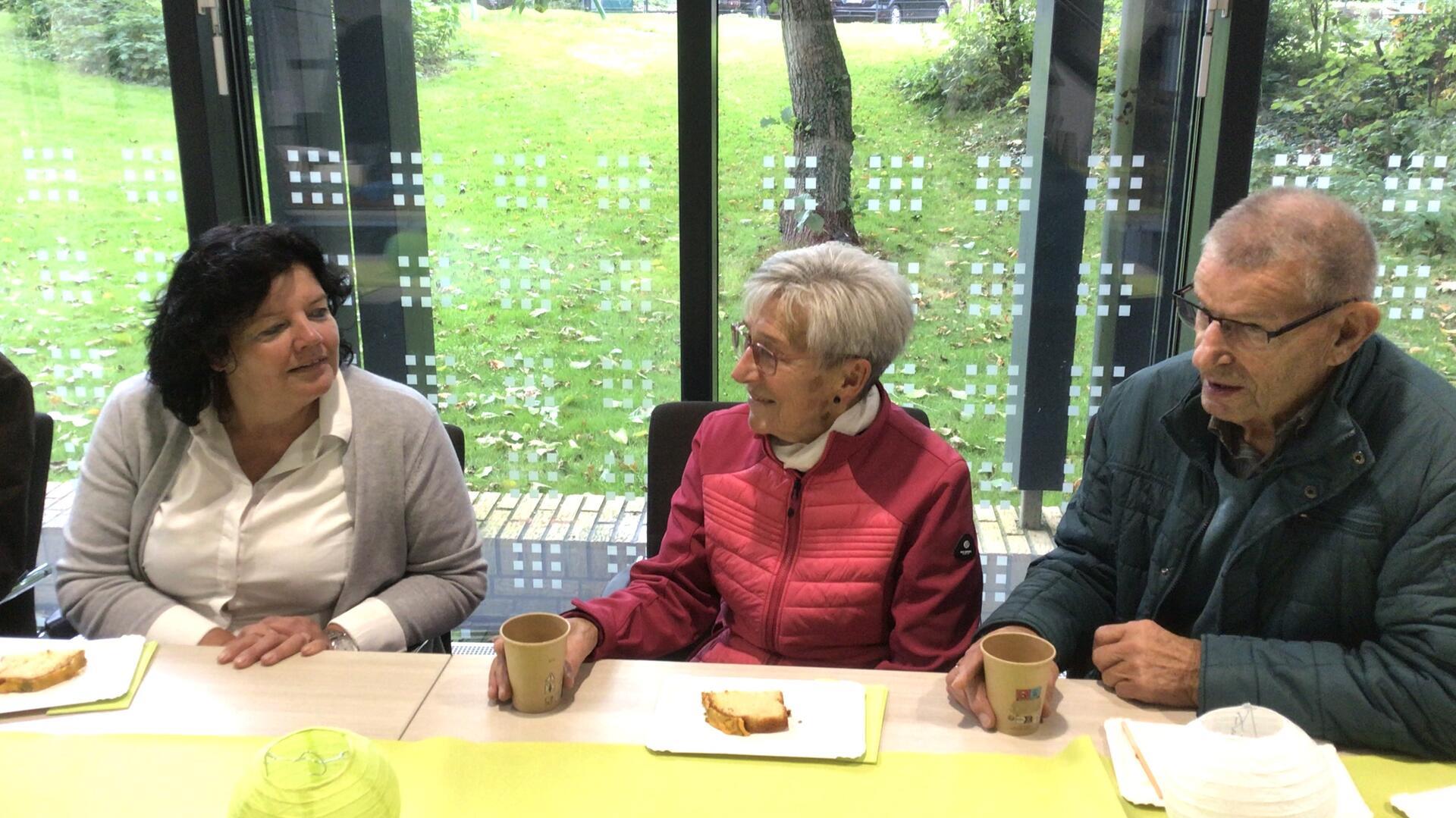 2 Frauen und ein Mann plaudern nebeneinander bei Kaffee und Topfkuchen.