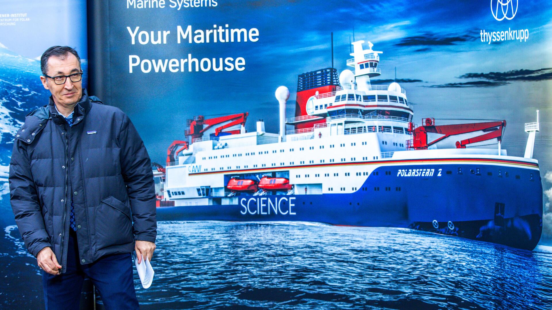 Ein Mann steht vor einem Plakat mit einem abgebildeten Schiff.