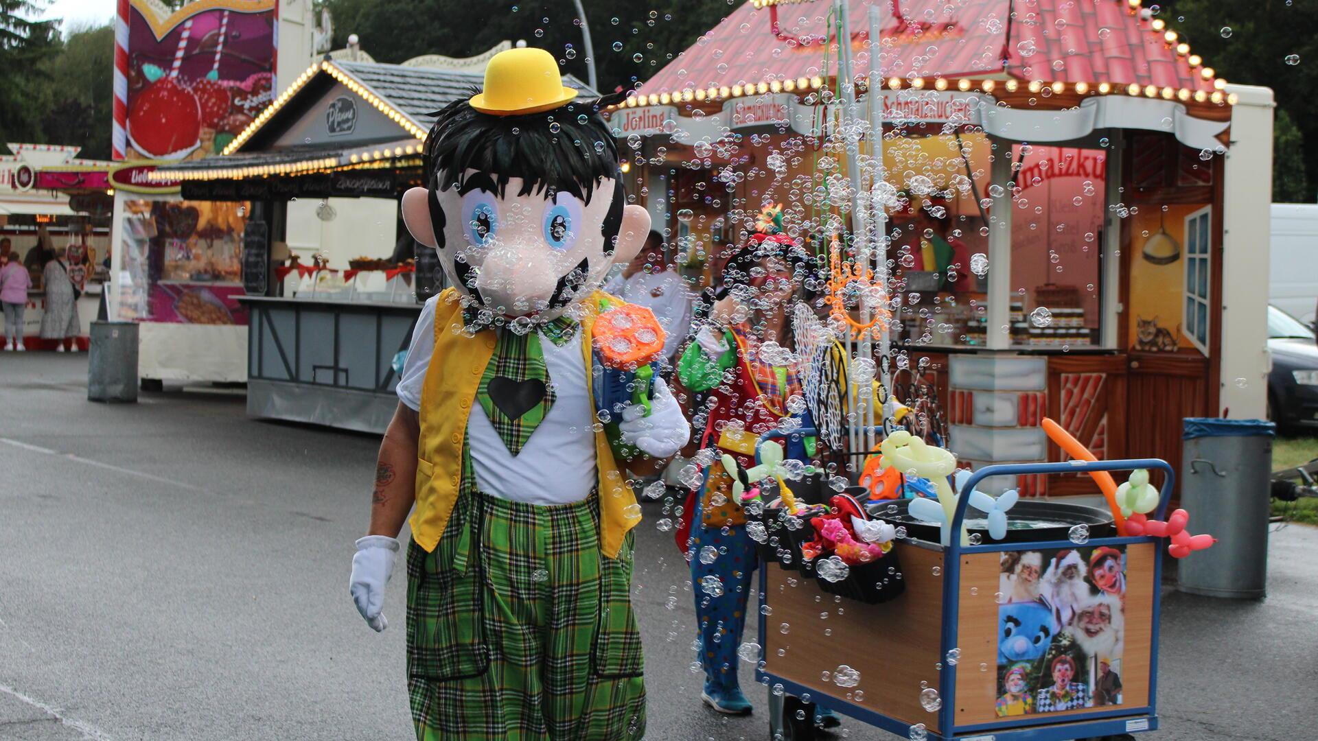 Maskottchen und Clown mit einem Wagen voller Luftballons.