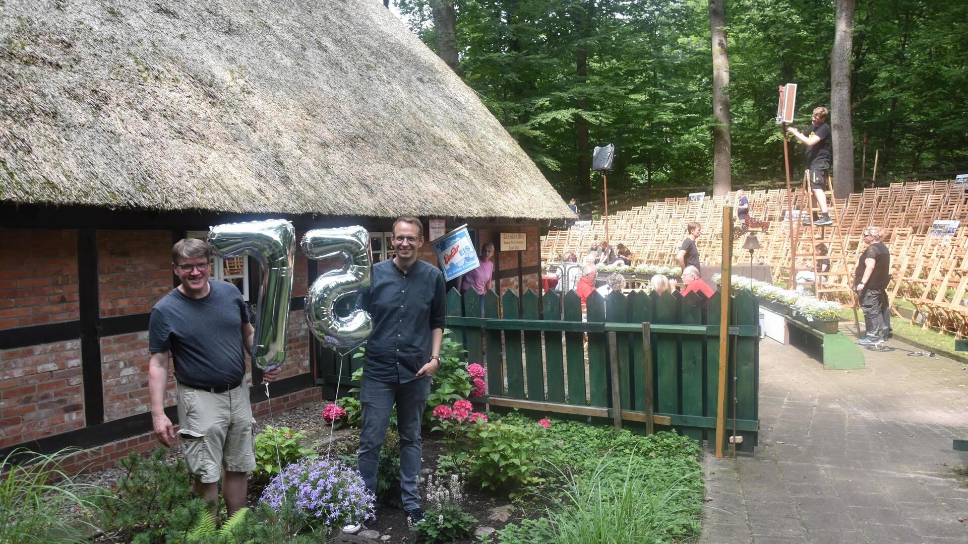 Zwei Männer stehen neben Folienluftballons mit den Ziffern 7 und 5.