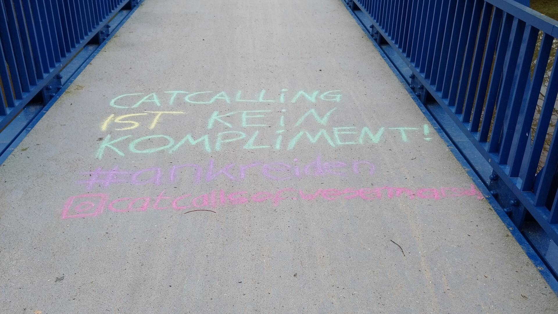 Eine Schrift mit Kreide auf einer Brücke mit blauem Geländer.