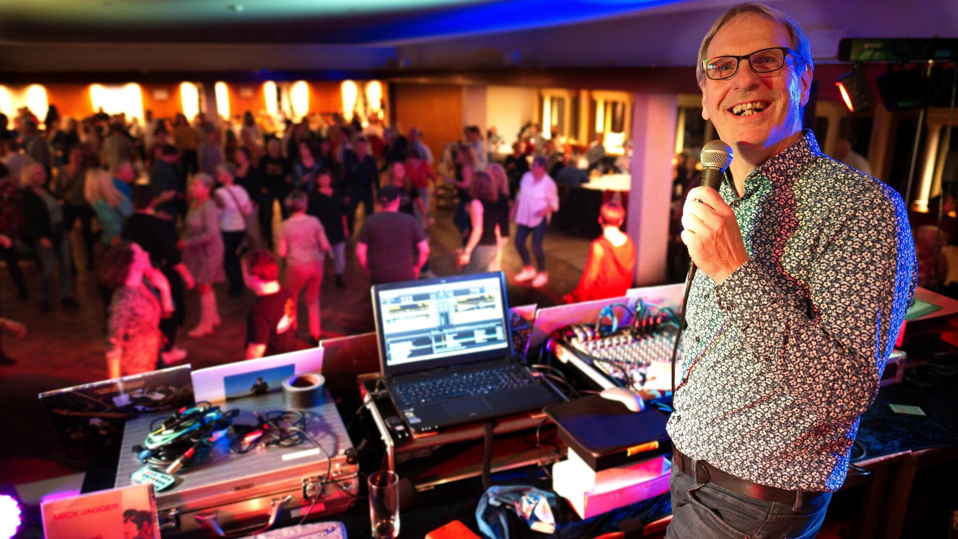 Ein DJ steht an seinem Mischpult vor der Menge tanzender Menschen.