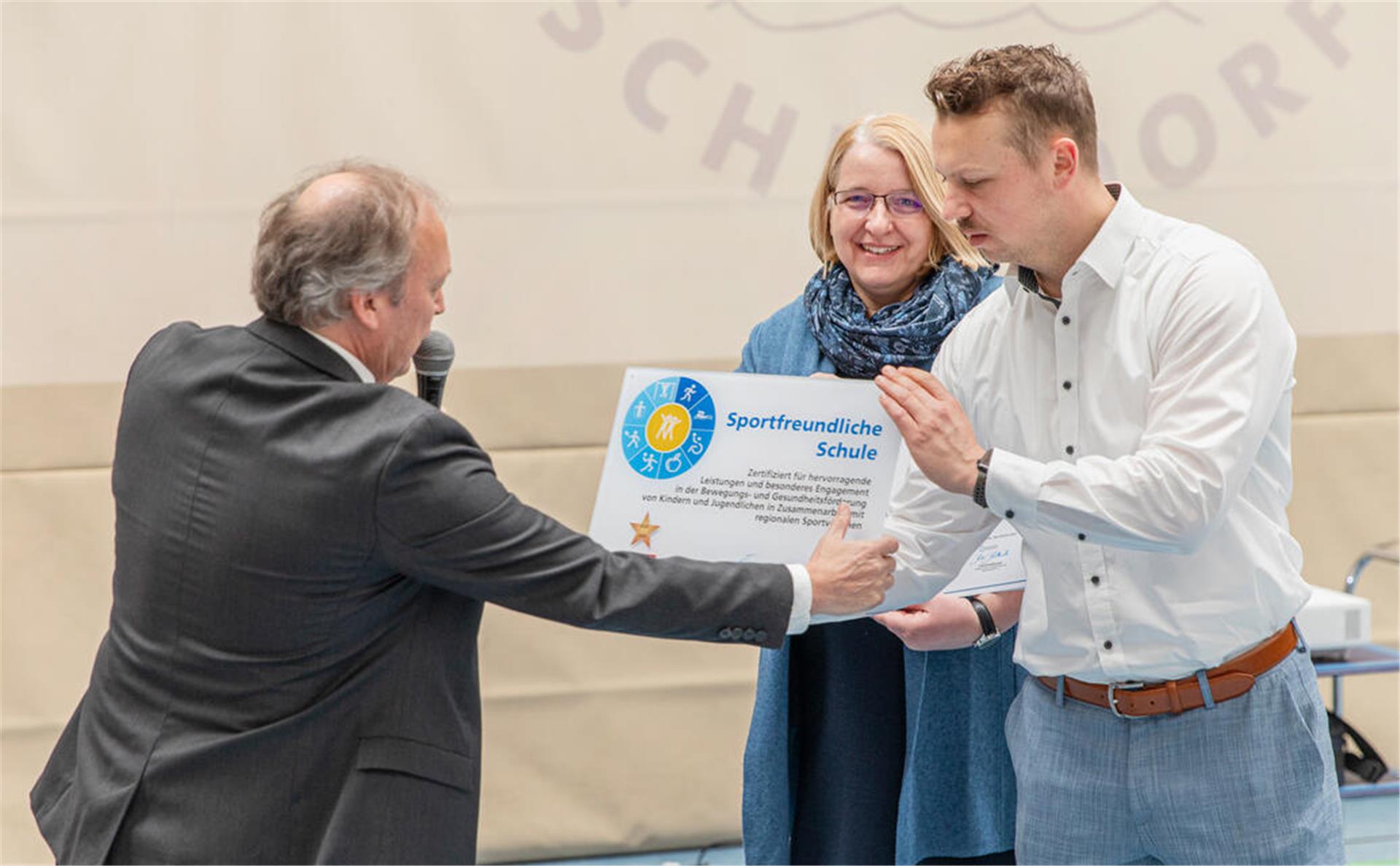 Detlef Zeidler (l.) überreicht das Zertifikat „sportfreundliche Schule“ an Sportlehrer Henry Bentin. Schulleiterin Maike Agit findet‘s gut.