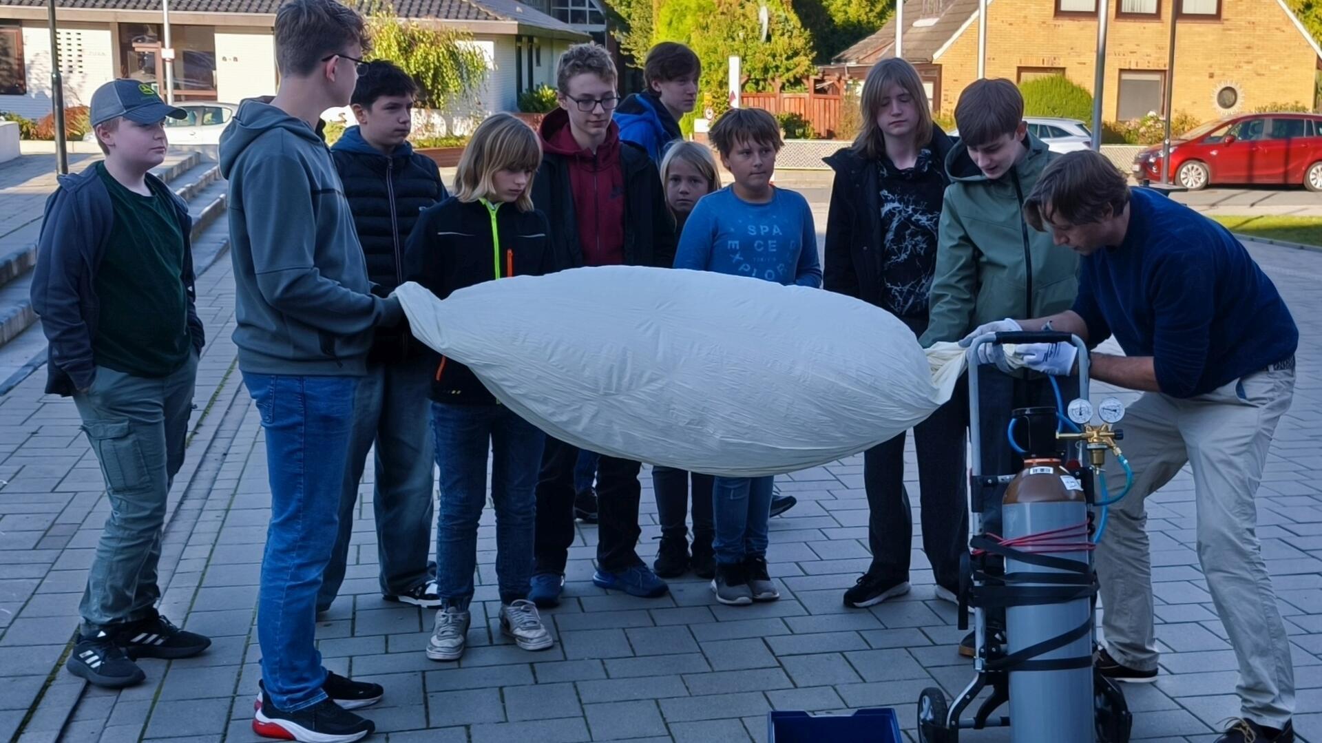 Mehrere Schüler und ein Lehrer  pumpen den Wetterballon auf.
