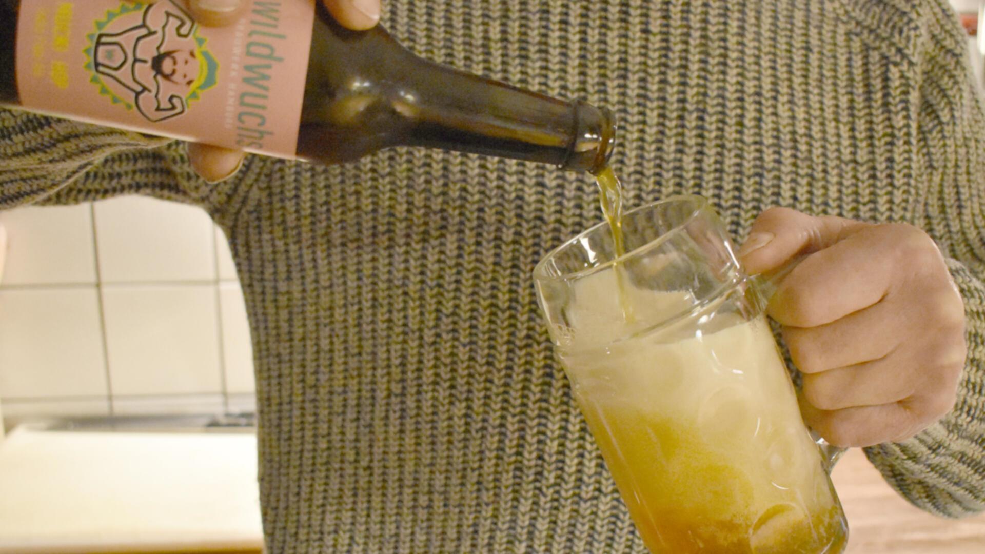 Eine Person schenkt ein Bier aus einer Flasche in ein Glas