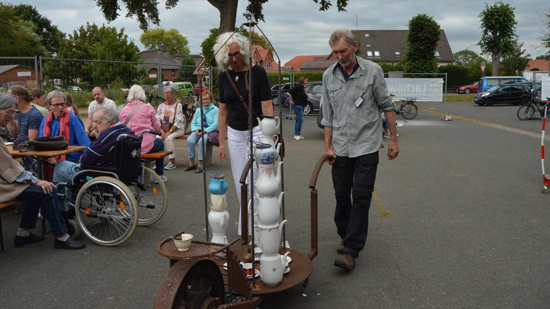Ein Mann schiebt eine Karre. Auf der Karre stehen Zusammengeklebte Kaffeekannen