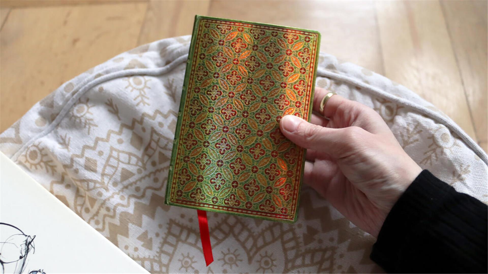 Hand hält Buch mit grünem Muster 