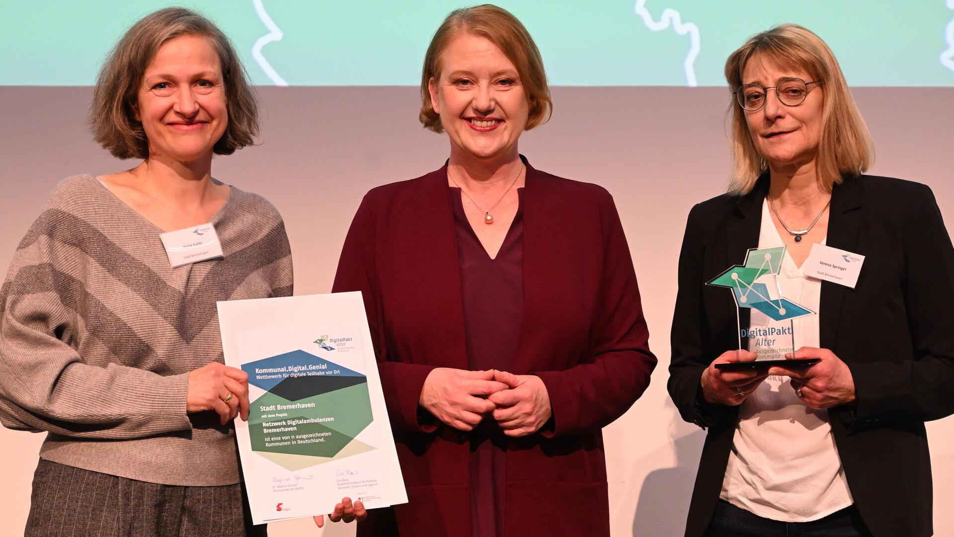 Gruppenfoto mit drei Frauen. Die Frau links hält eine Urkunde in der Hand, die Frau rechts eine Auszeichnung. Das Netzwerk Digitalambulanzen Bremerhaven zählt zu den Gewinnern des bundesweiten Wettbewerbs „Kommunal.Digital.Genial“: Heike Eulitz (links) und Verena Springer (rechts) nahmen die Auszeichnung im Beisein von Bundesseniorenministerin Lisa Paus in Mannheim entgegen.