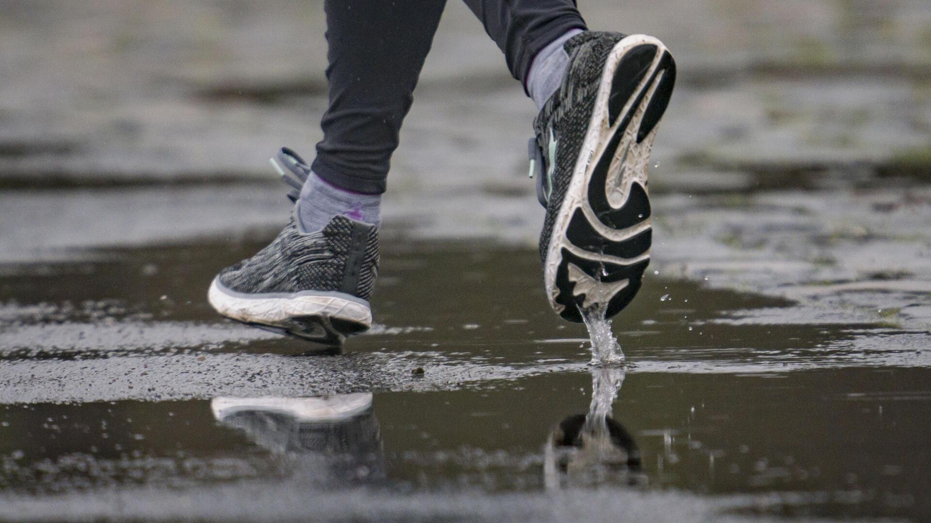 Die Füße eines Joggers spiegeln sich in einer Pfütze.