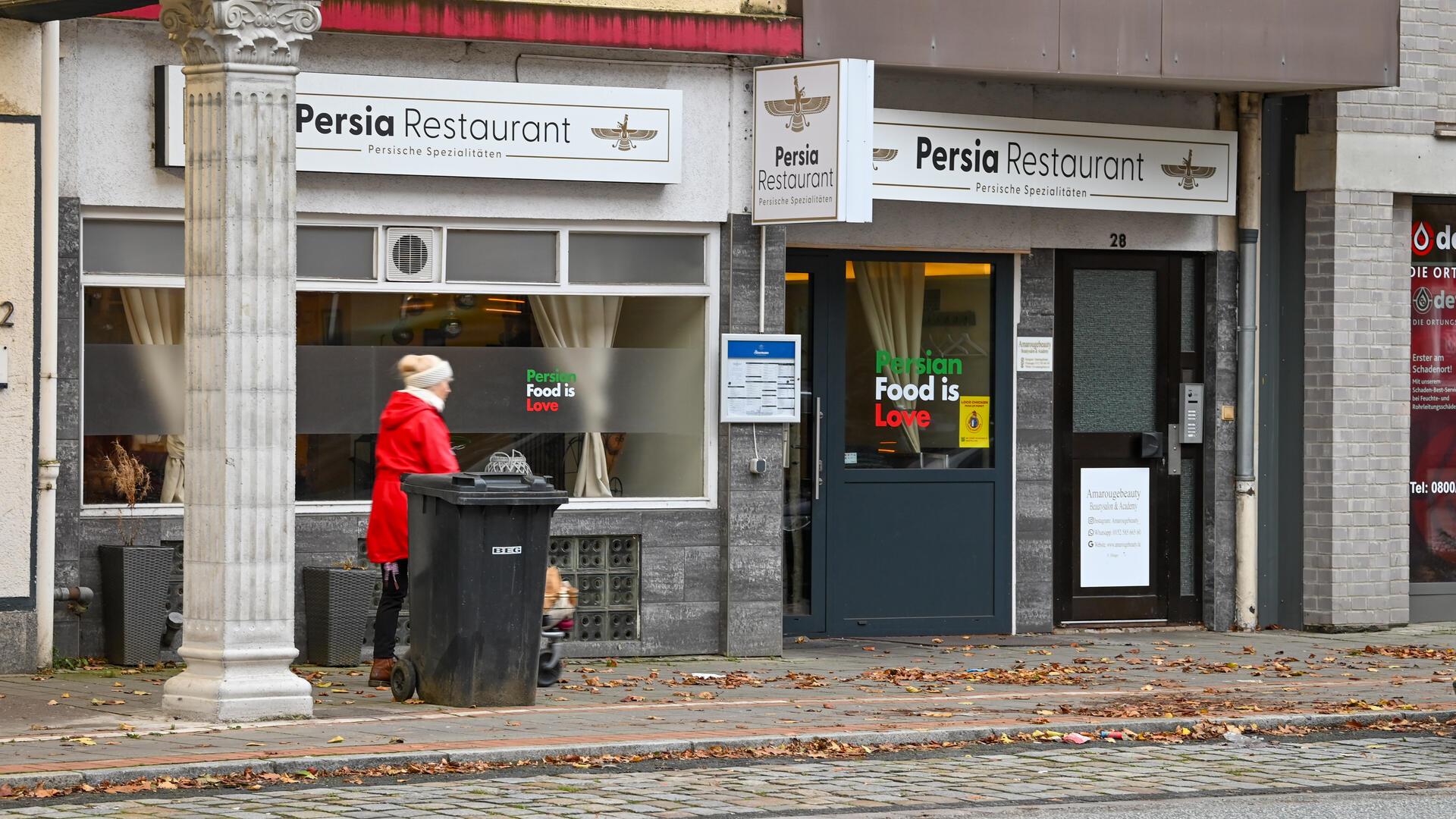 Eine Häuserfassade: An ihr steht der Schriftzug "Persia Restaurant". Eine Frau mit roter Jacke läuft am Eingangsbereich vorbei.