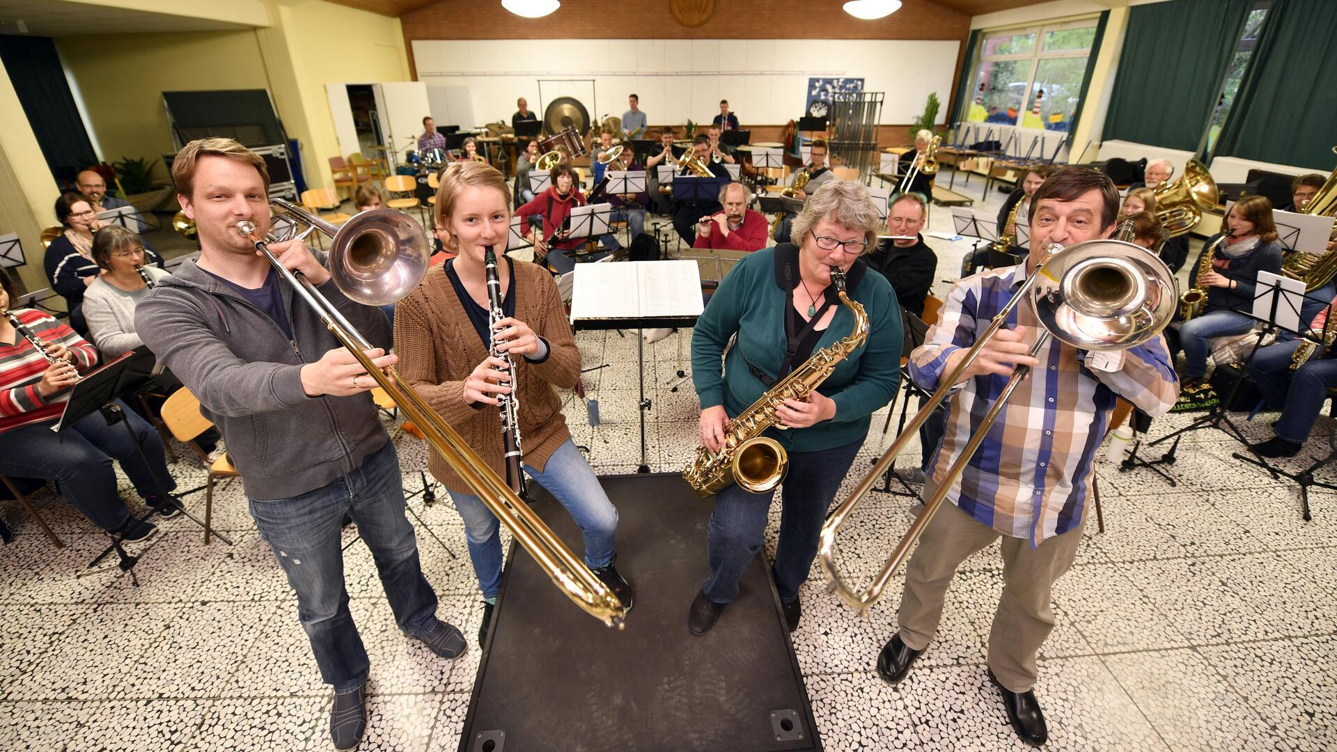 Musikerinnen und Musiker des Sinfonischen Blasorchesters Wehdel proben gemeinsam in einem Saal. Im Vordergrund spielen zwei Posaunisten, eine Klarinettistin und eine Saxofonistin, während im Hintergrund das gesamte Orchester mit Blech‑, Holzbläsern und Schlagwerk zu sehen ist.