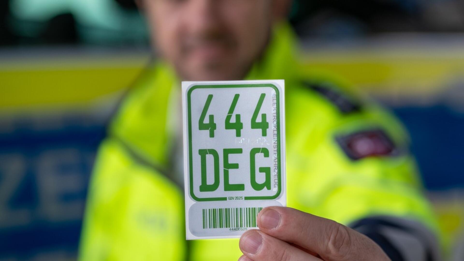 Ein Polizist hält eine grüne Plakette für Kleinfahrzeuge vor die Kamera.