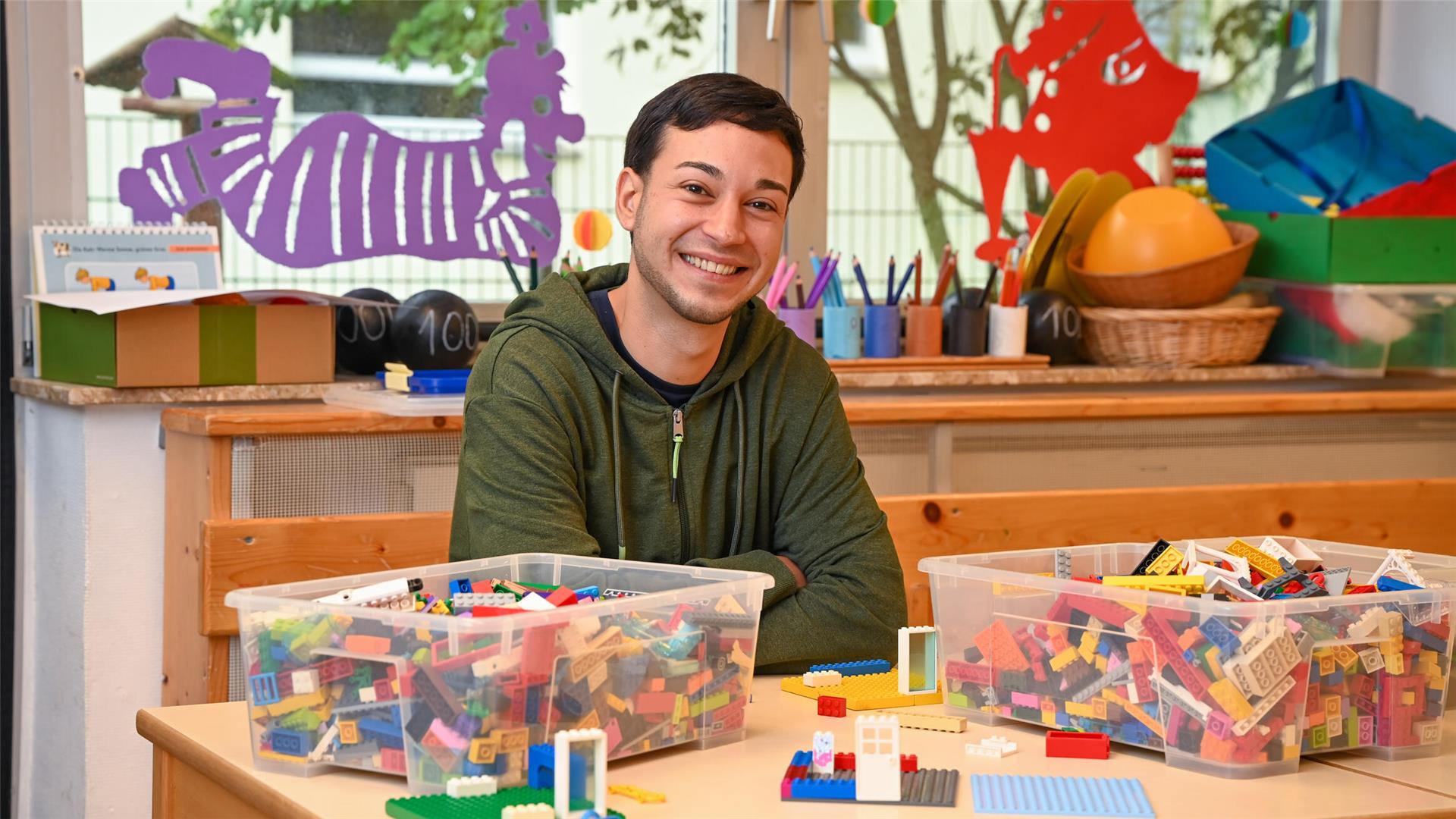 Ein junger Erzieher hinter einem Tisch mit Lego-Steinen. 