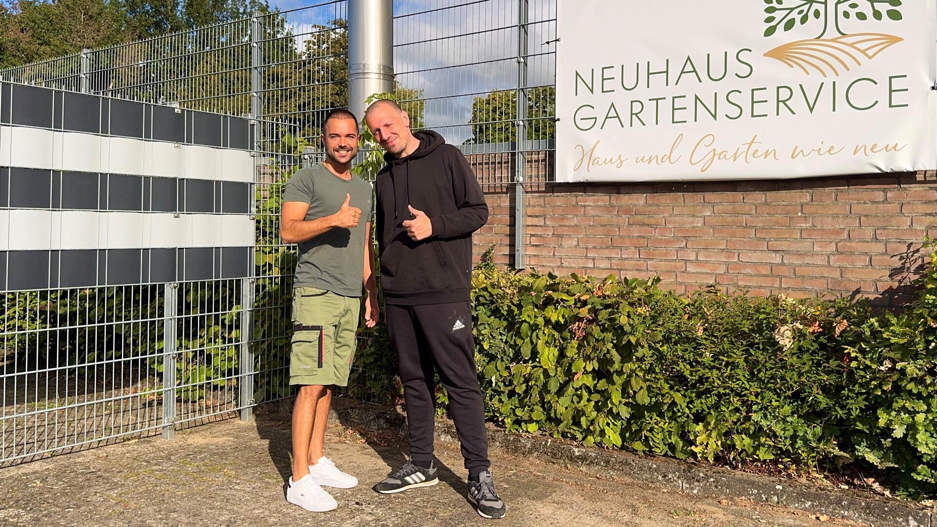 Zwei junge Herren stehen vor einem Gebäude, lächeln in die Kamera und halten einen Daumen nach oben.
