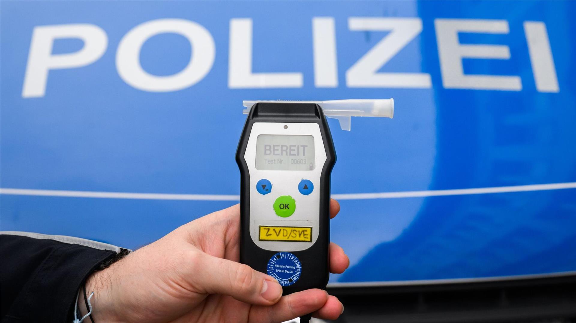 Ein Schriftzug Polizei und ein kleines Gerät in einer Hand.