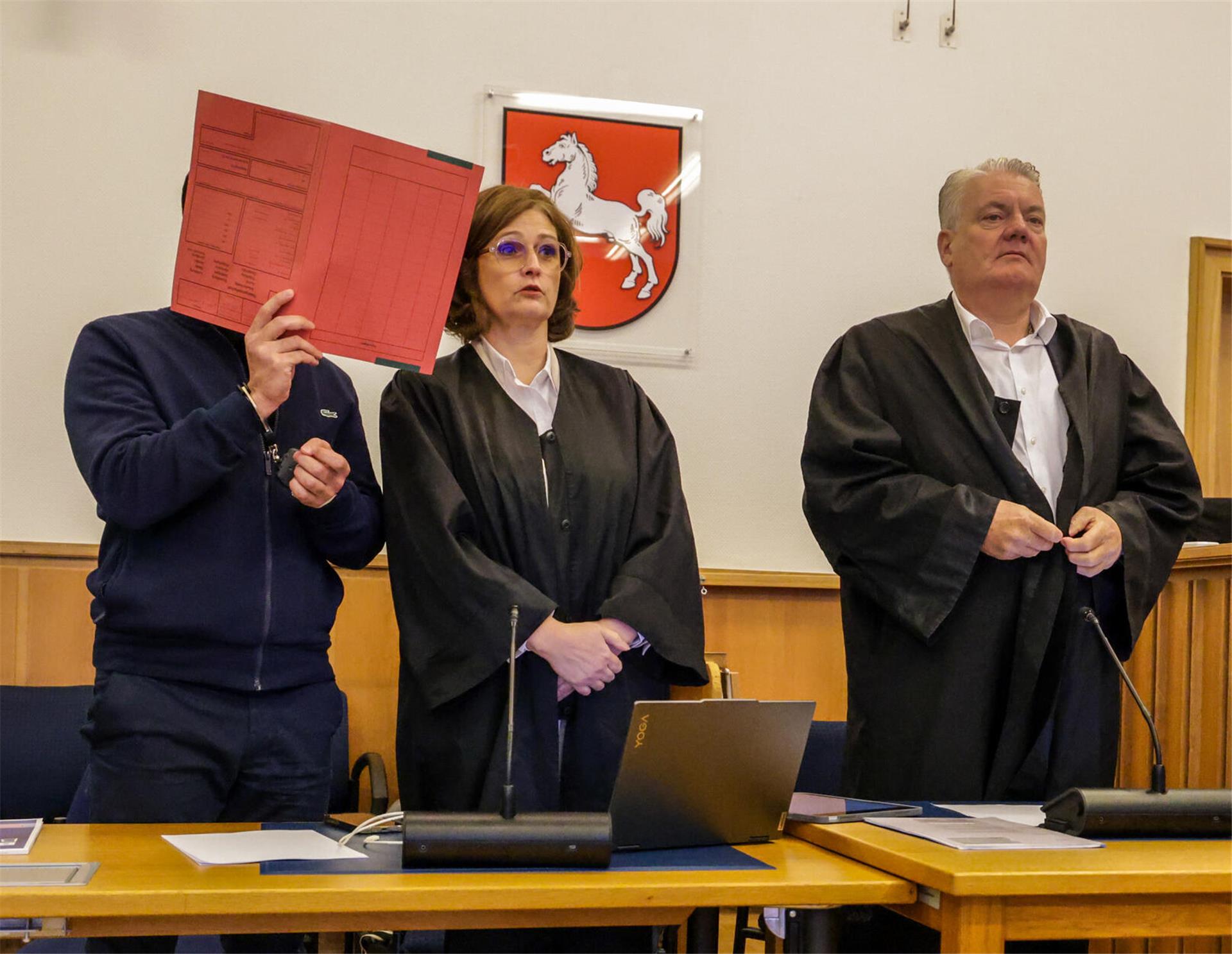Der Angeklagte steht mit einem Aktenordner vor dem Gesicht neben seinen Verteidigern Dinah Busse und Dirk Meinicke (rechts) im Saal des Landgerichts Stade. Dem Angeklagten wird vorgeworfen, im März 2024 einen 35-Jährigen mit einem Messerstich in den Kopf getötet zu haben. 