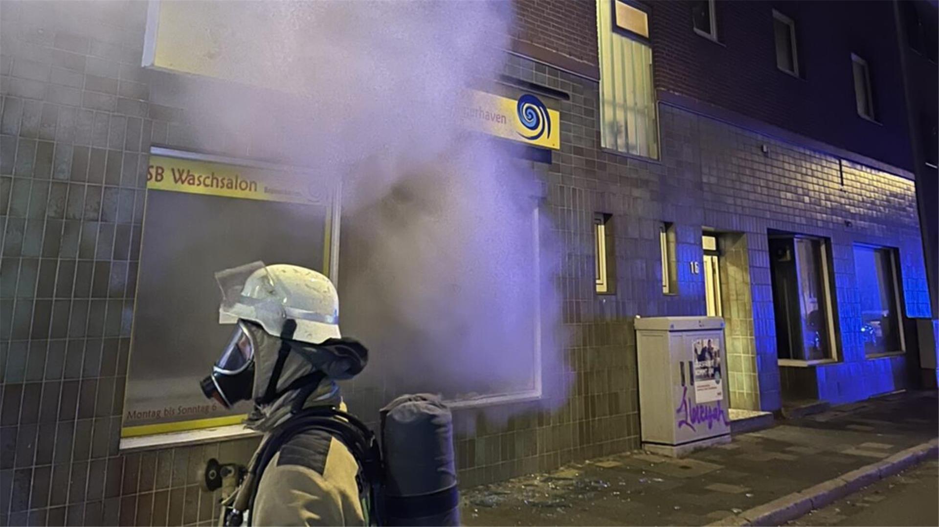Ein Feuerwehrmann steht vor einem qualmenden Waschsalon.