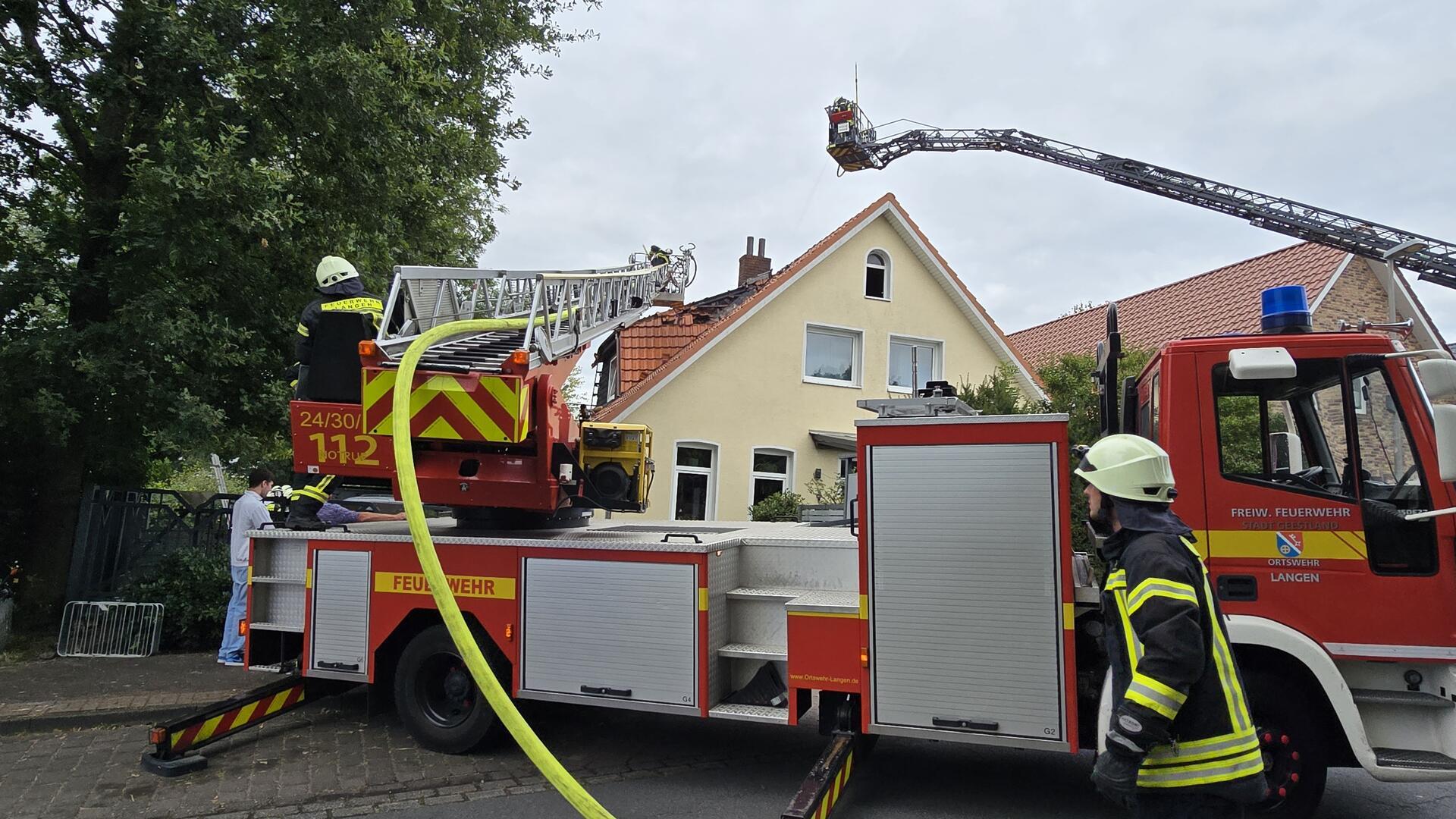 Eine Feuerwehr-Drehleiter steht vor einem Wohnhaus mit Ziegeldach, das rote Ziegeldach ist nach einem Feuer aufgerissen