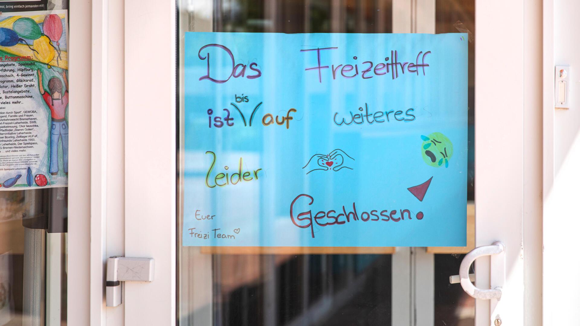Ein Schild mit bunter Schrift hängt an einer Glastür.