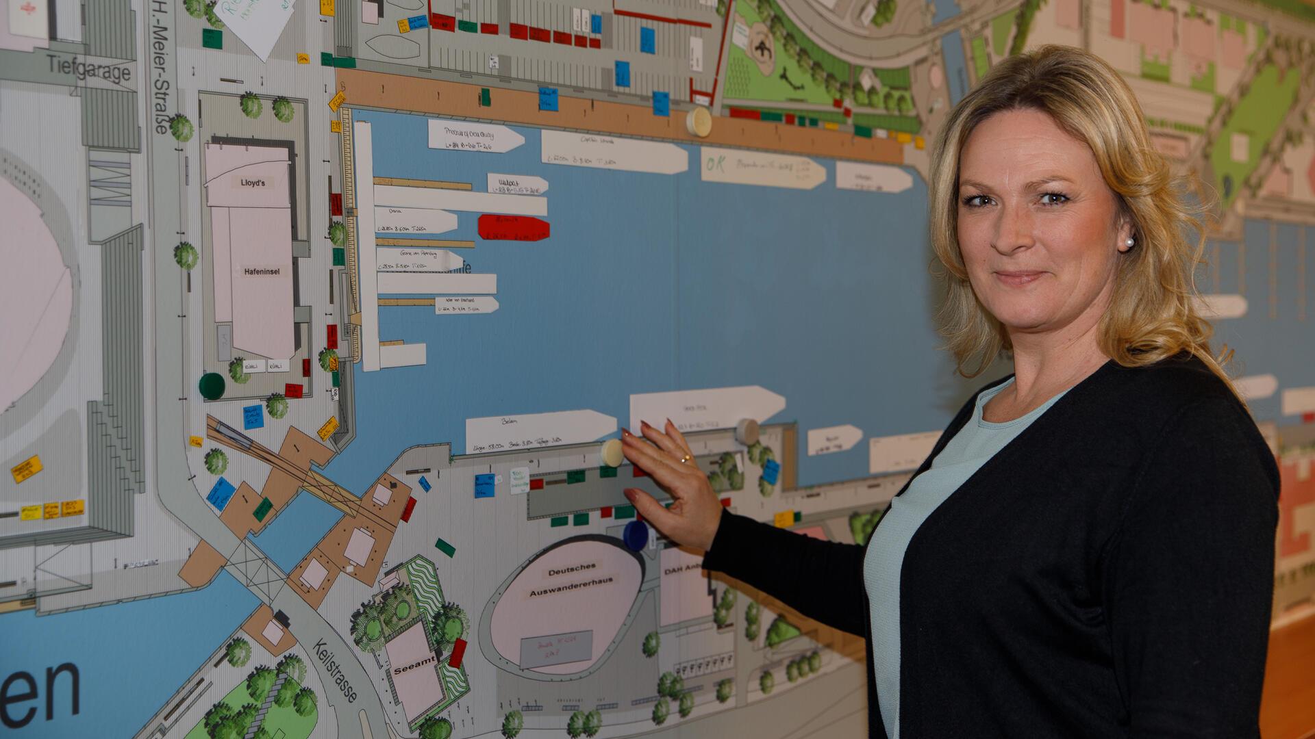 Karolin Meier steht vor einer Karte des Neuen Hafens. Sie ist als Marktmeisterin für die Organisation der Sail 2025 im Einsatz.