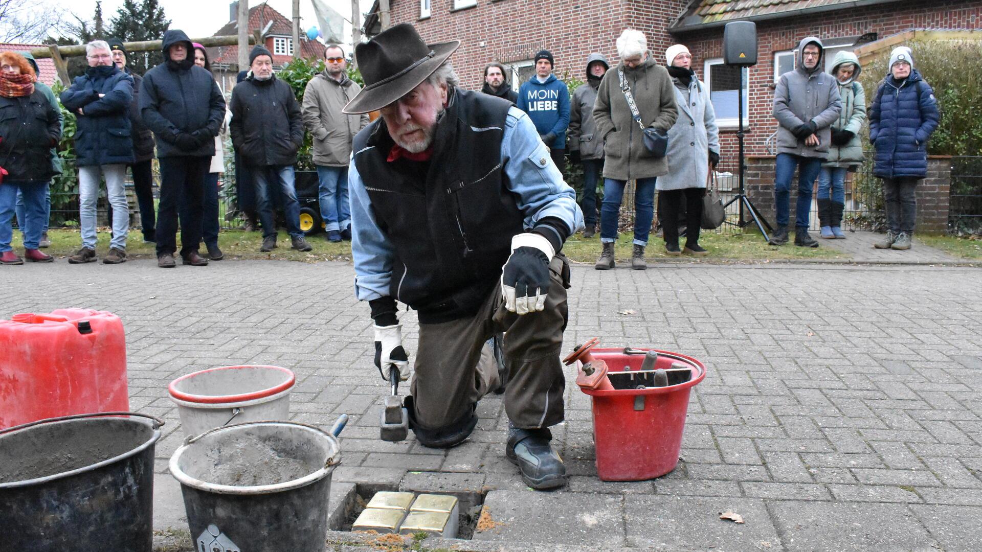 Ein alter Mann kniet auf einer Straße und verlegt Pflastersteinen.