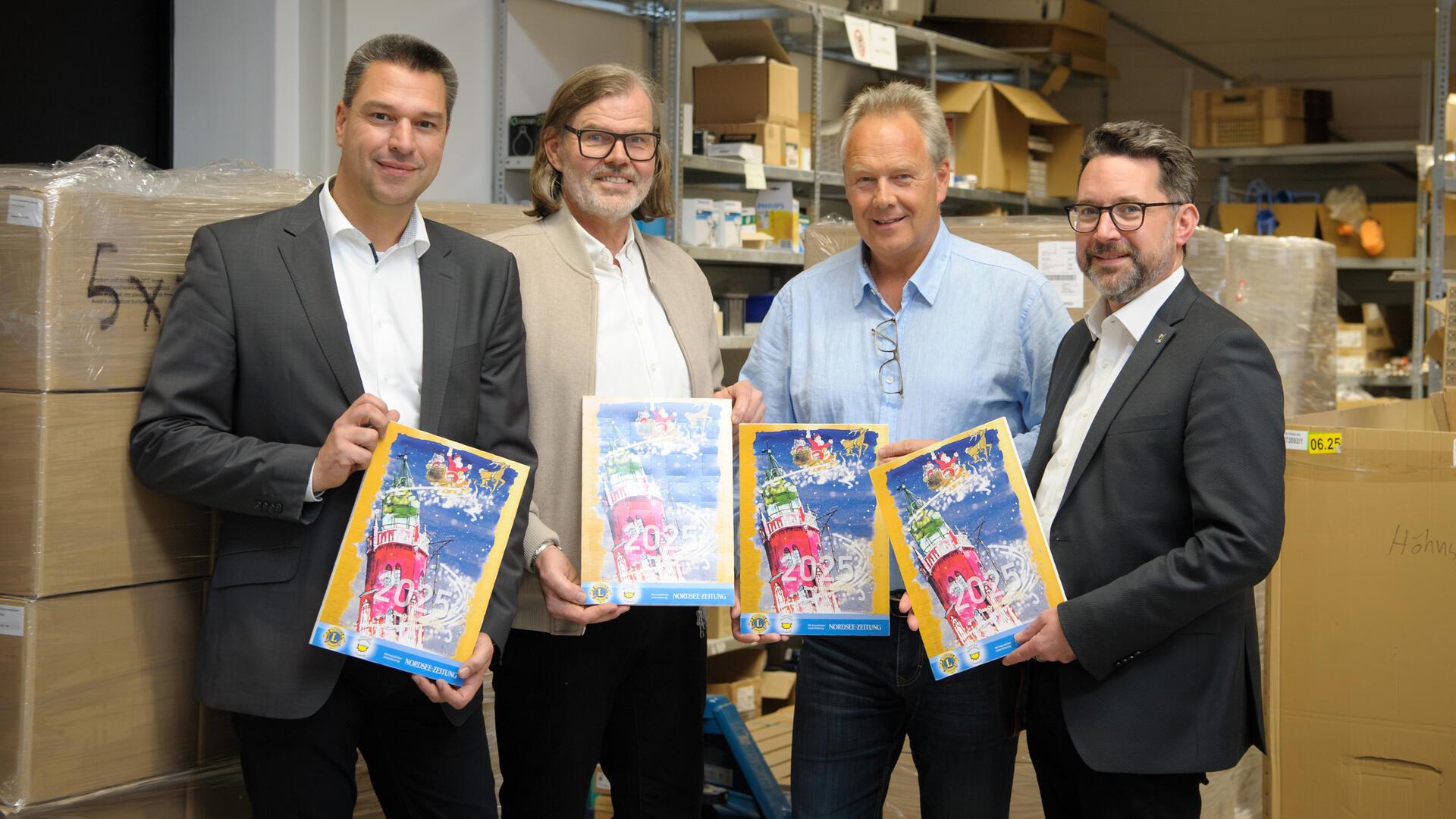 Der Adventskalender des Lions Club Bremerhaven Carlsburg: Bald erhältlich Vier Männer mit jeweils einem Adventskalender in der Hand stehen in einem Lager vor Kartons.