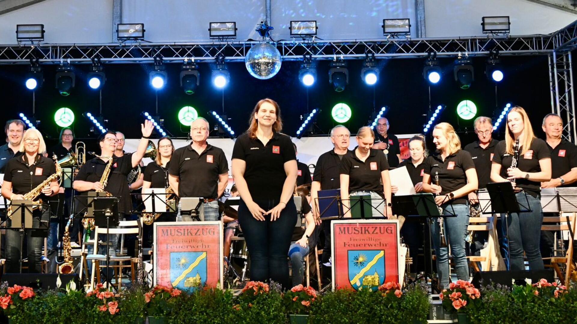 Männer und Frauen in schwarzen Poloshirts stehen auf einer beleuchteten Bühne in einem Festzelt