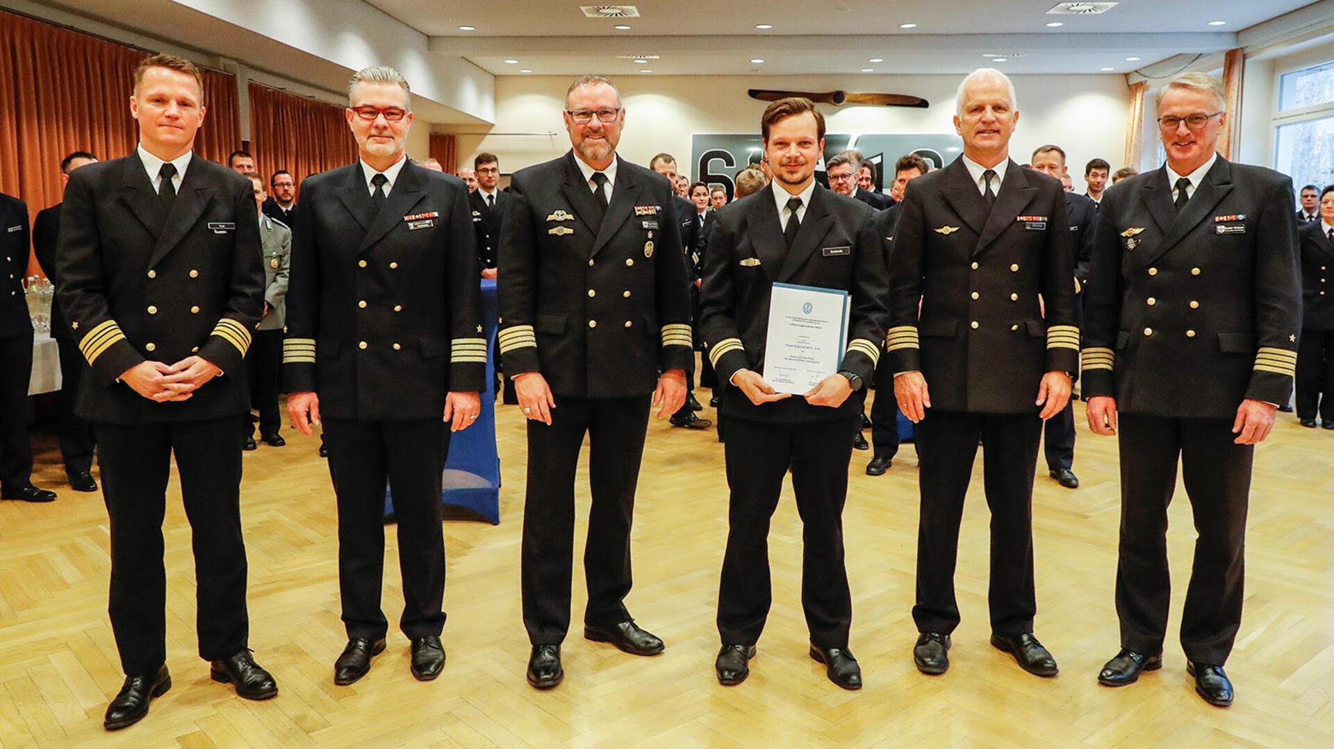 Der Preisträger, Kapitänleutnant Pascal Budzinski (3.v.r) wird umrahmt (v.l.) von Fregattenkapitän Christian Inan, Kommodore des MFG 5, Kapitän zur See Carsten Holtgreve, dem Chef des Stabes, Kapitän zur See Holger Schmitt, dem Kommodore des MFG 3, Kapitän zur See Oliver Ottmüller und Marineflieger-Kommandeur, Kapitän zur See Broder Nielsen.