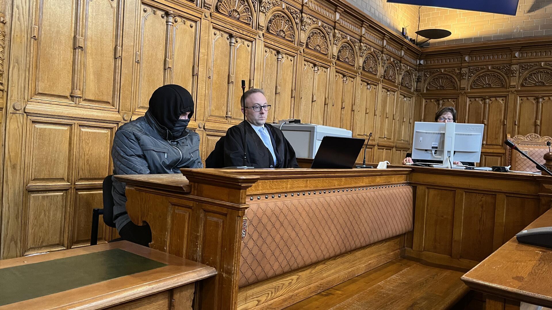 Mann mit Maske sitzt auf der Anklagebank. 