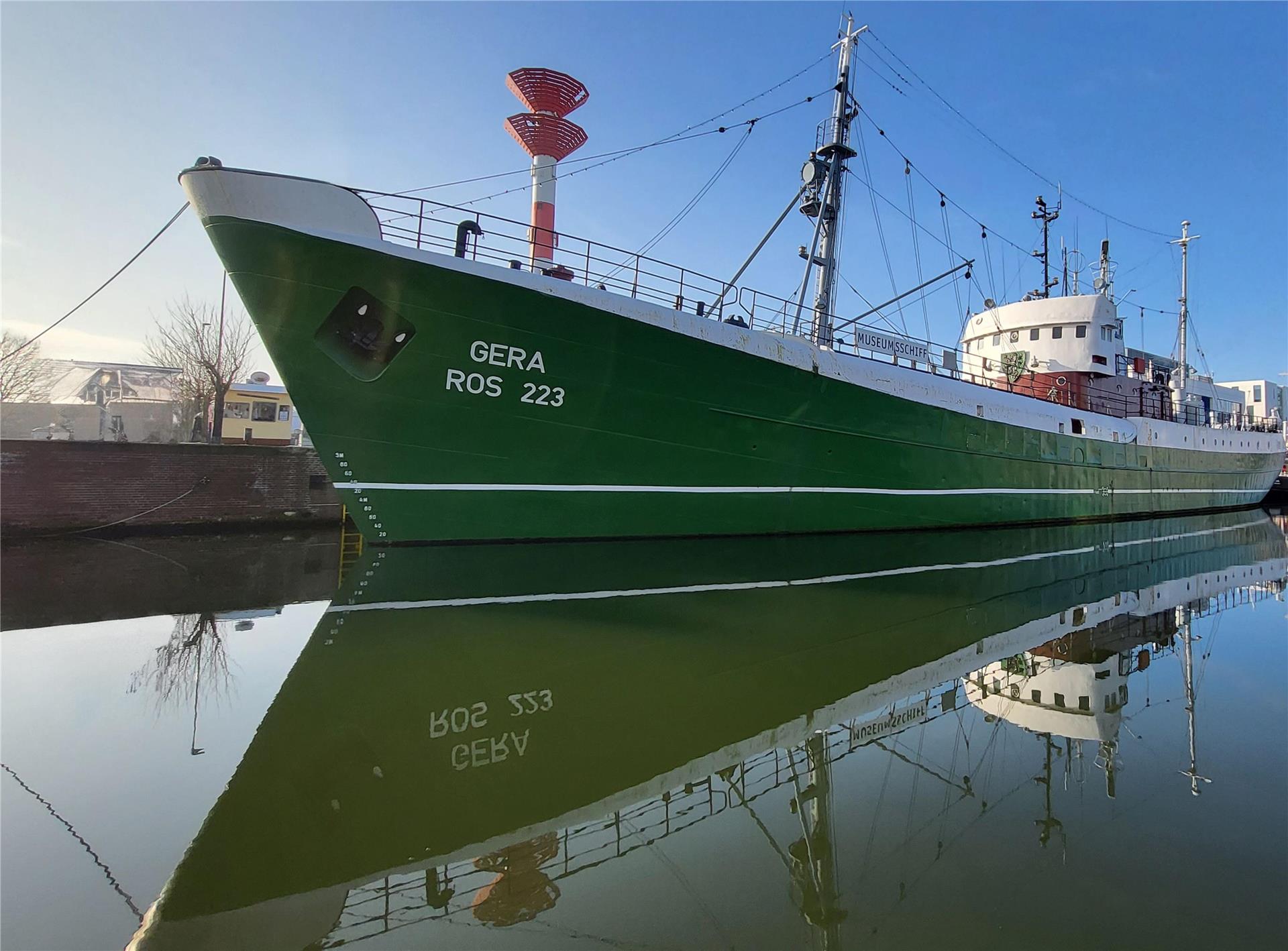 Ein Schiff liegt an der Kaje. Im Wasser spiegelt sich der Rumpf.