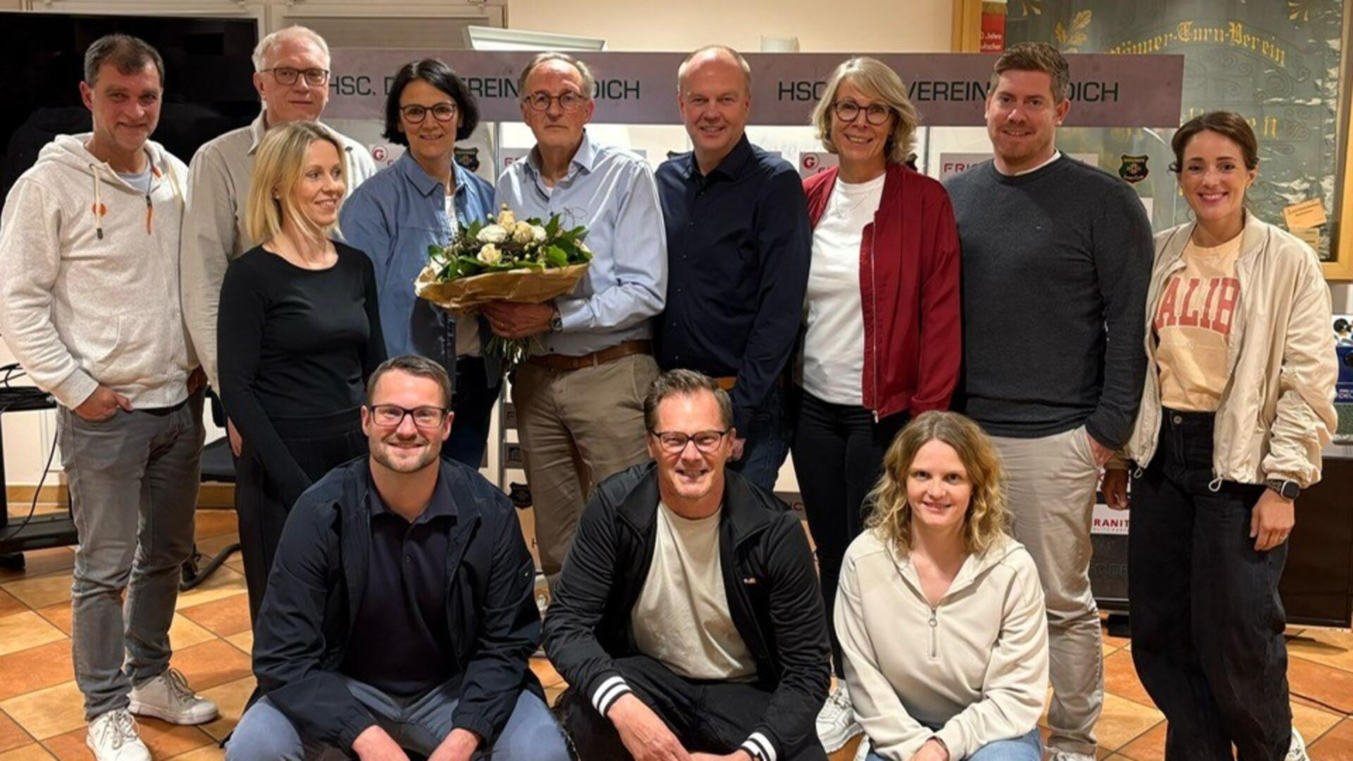 Zwölf Männer und Frauen stehen und hocken in zwei Reihen vor der Kamera.