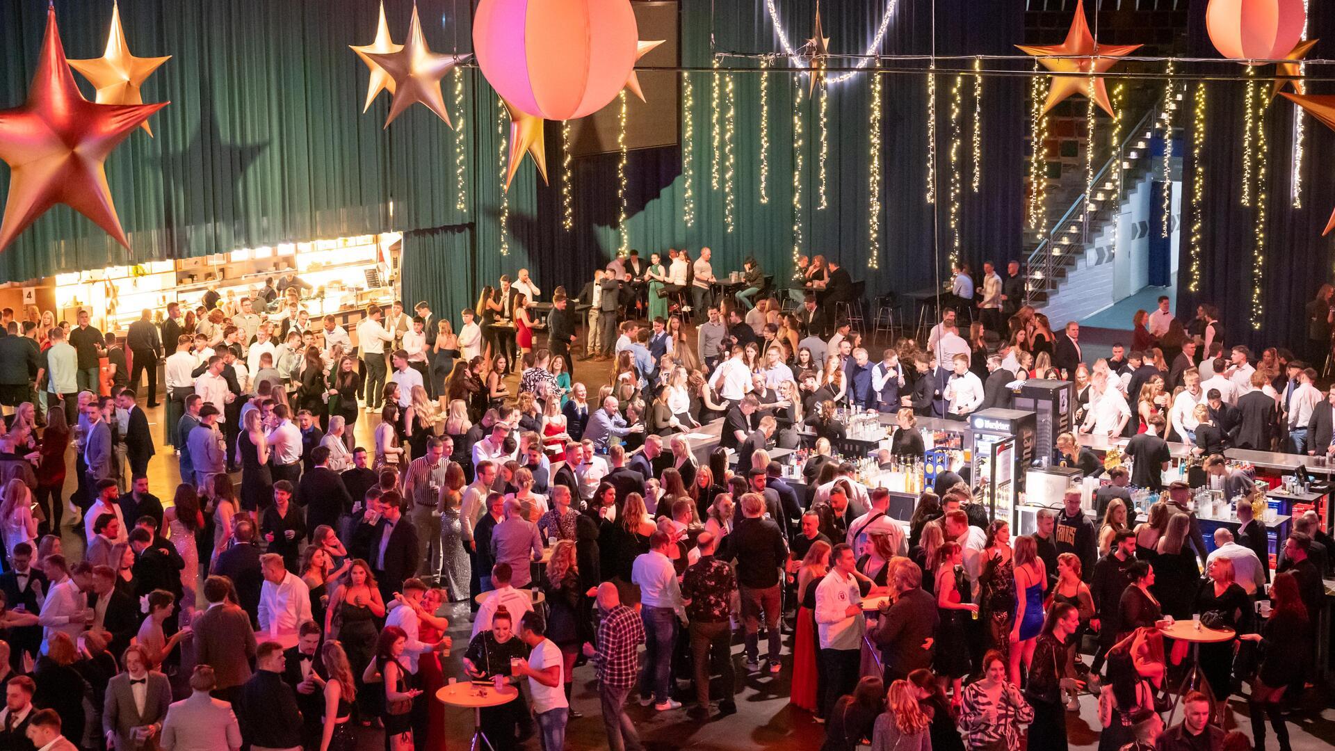 Viele Menschen stehen in einer weihnachtlich geschmückten Halle und feiern.