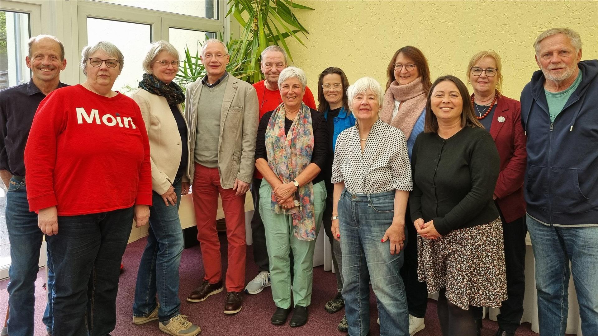 Männer und Frauen stehen in einer Gruppe zusammen und gucken in die Kamera