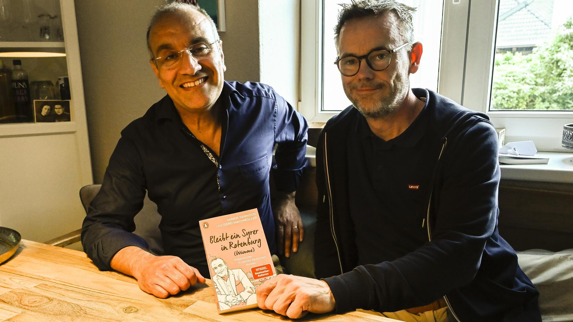 Zwei Männer sitzen an einem Tisch, lächeln und zeigen ein Buch. Der dritte Band der Trilogie von Samer Tannous (links) und Gerd Hachmöller soll die letzte gemeinsame Veröffentlichung der Kolumnen sein.