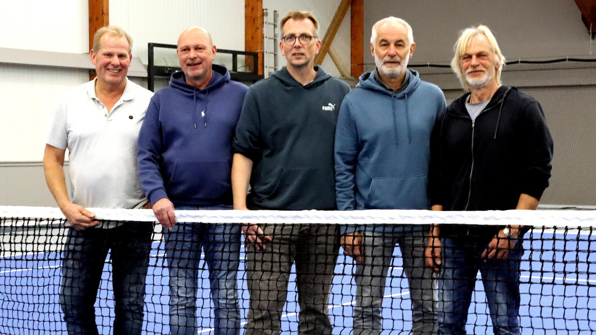 Fünf Männer stehen hinter einem Tennisnetz und lächeln in die Kamera.