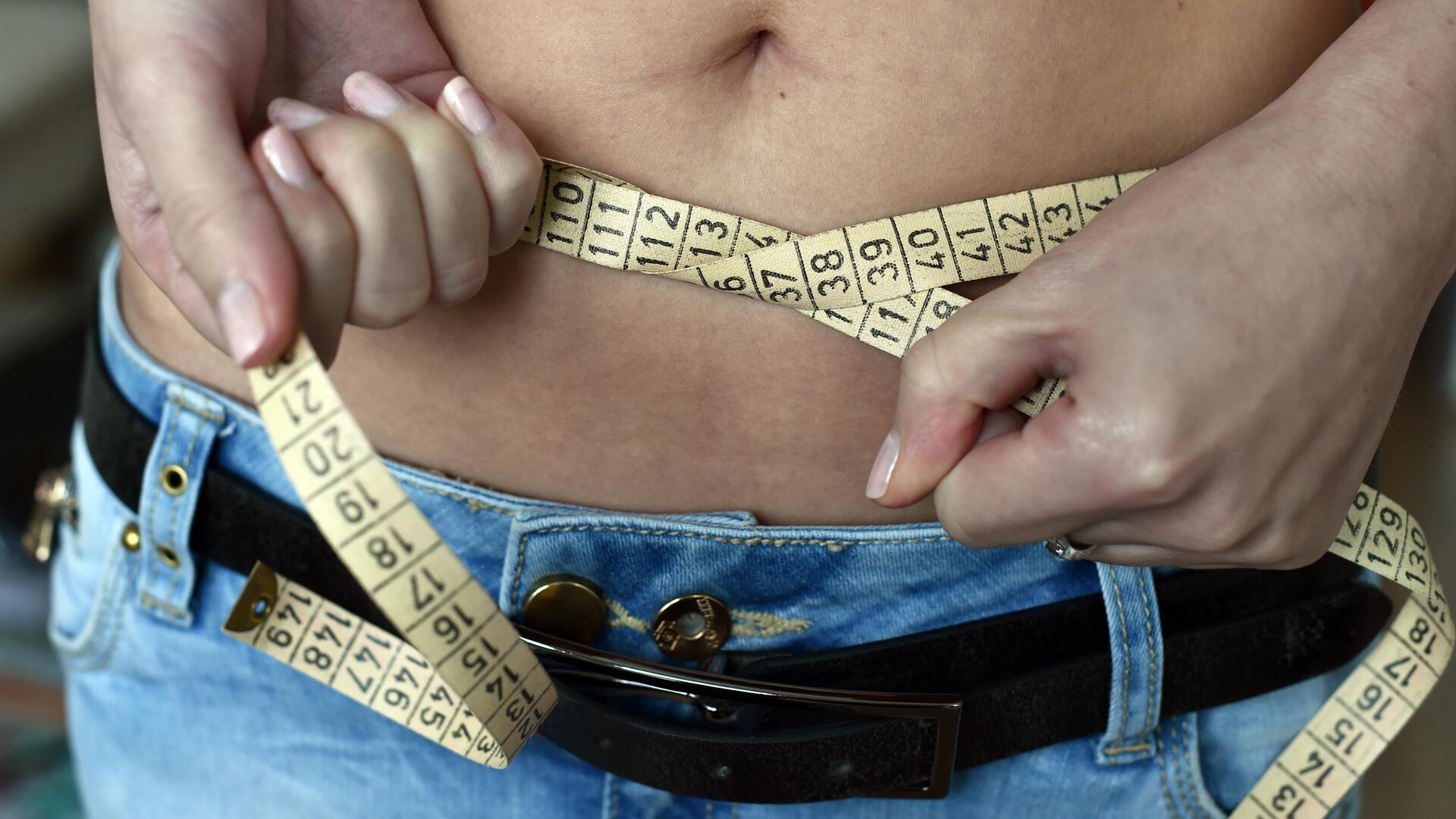 Eine junge Frau legt ein Maßband um ihren Bauch