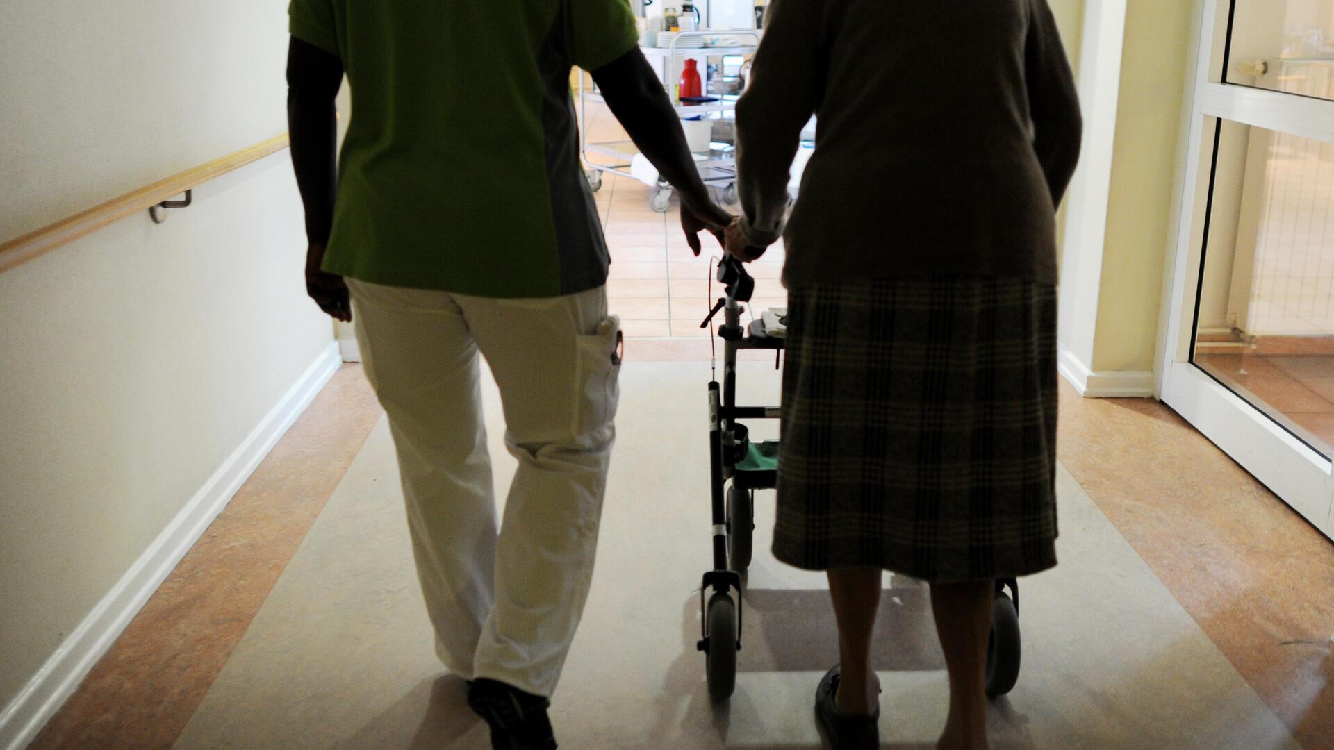 Eine Pflegekraft läuft neben einer Frau mit Rollator.