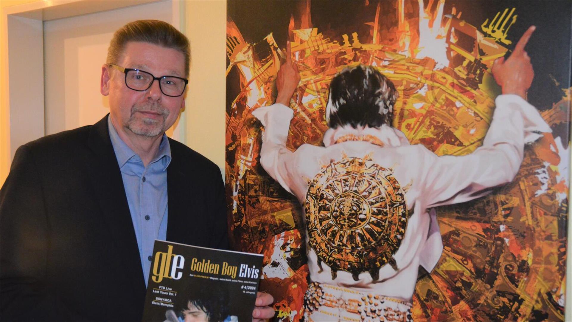Ein Mann mit einem Magazin in der Hand steht neben einem großen Elvis-Bild.