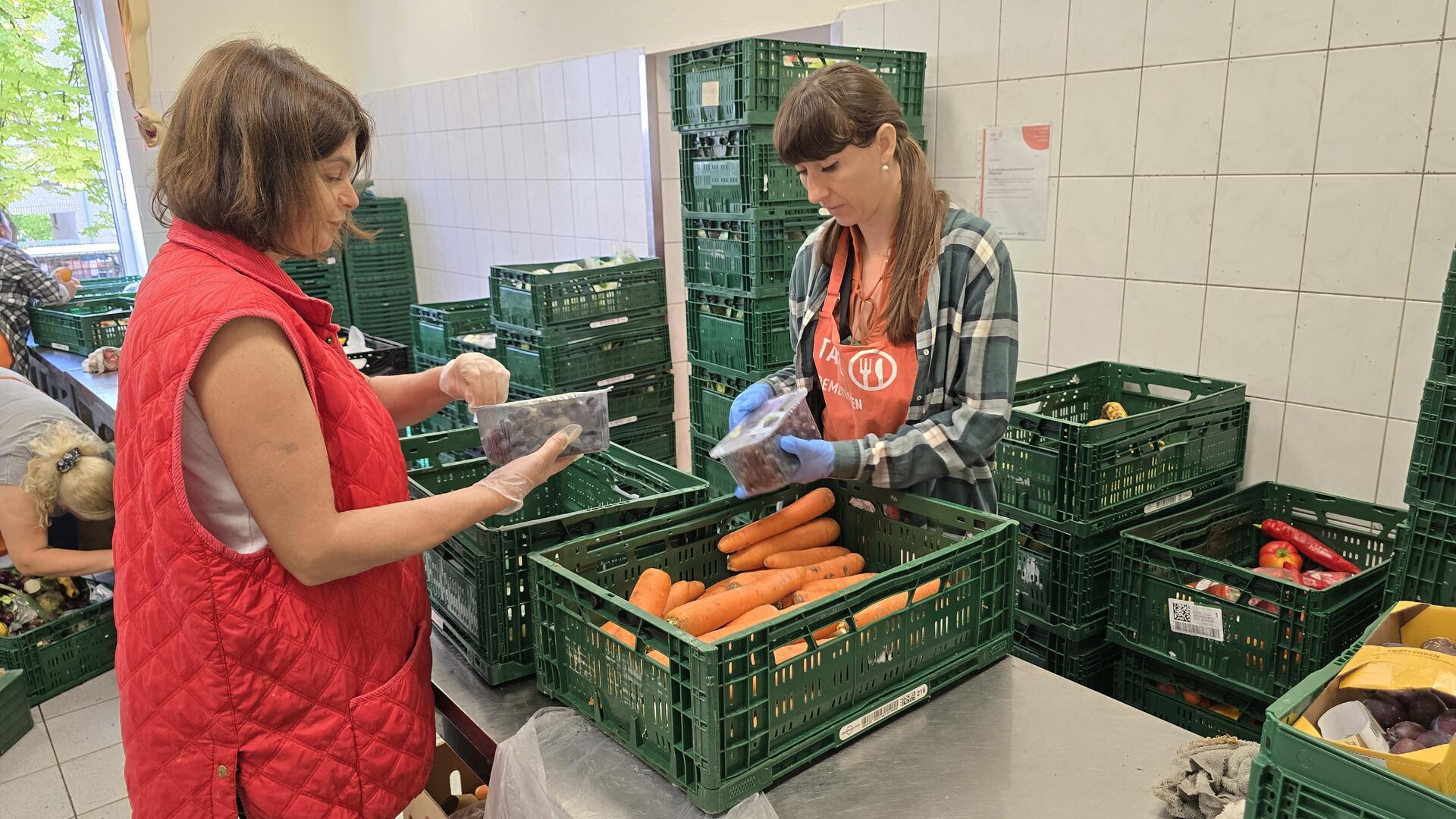Zwei Frauen sortieren Obst und Gemüse in einem Raum, der voller grüner Kisten steht