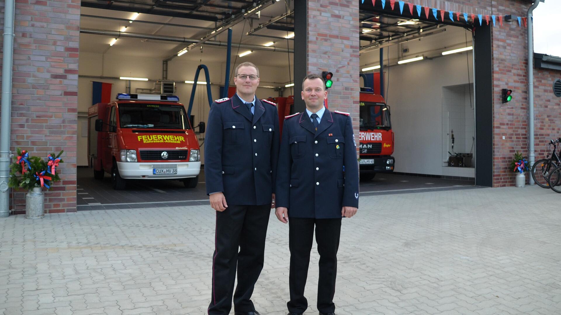 2 Männer in Uniform vor Haus mit Feuerwehrfahrzeugen
