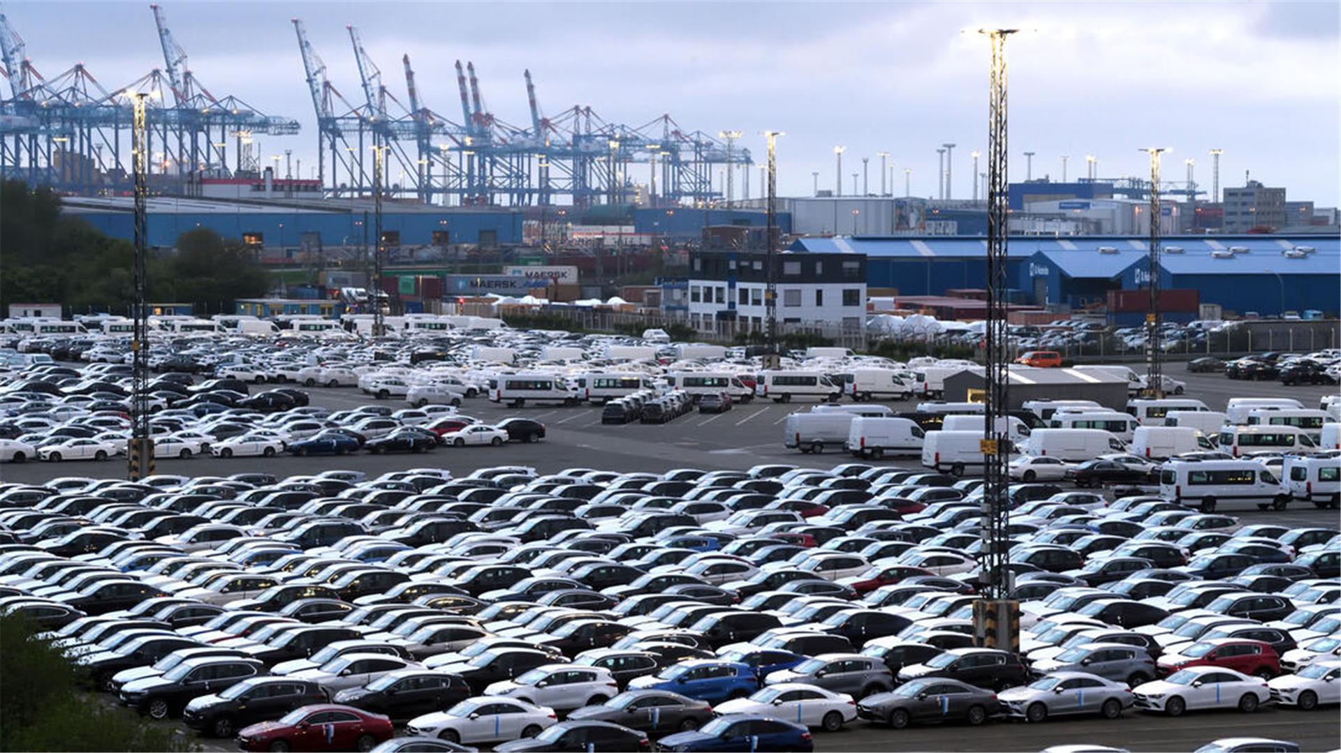 Geparkte Autos und Containerbrücken im Hintergrund.