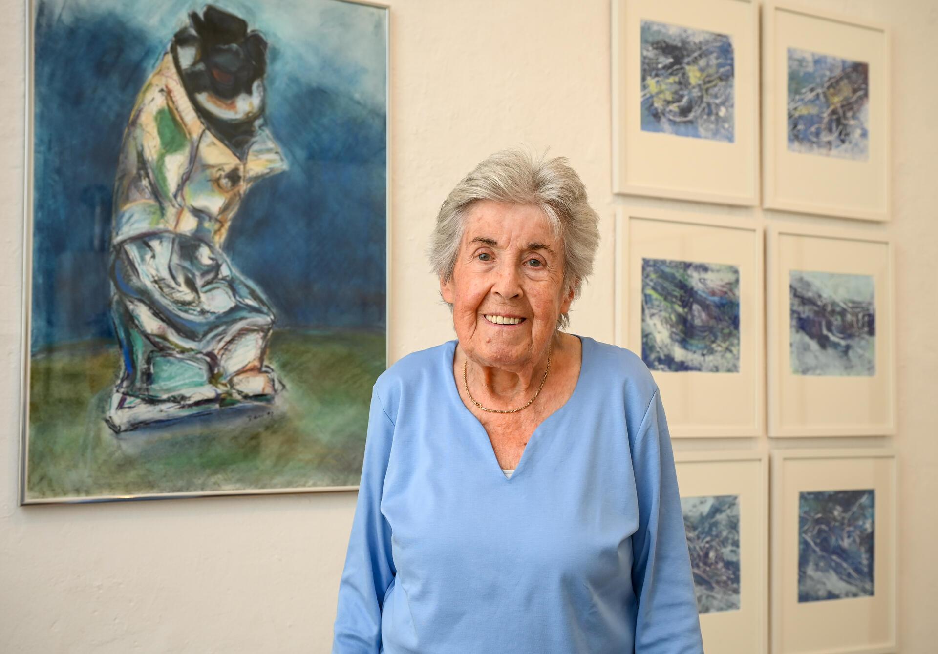 Eine Frau steht vor einer mit Bildern behängten Wand.