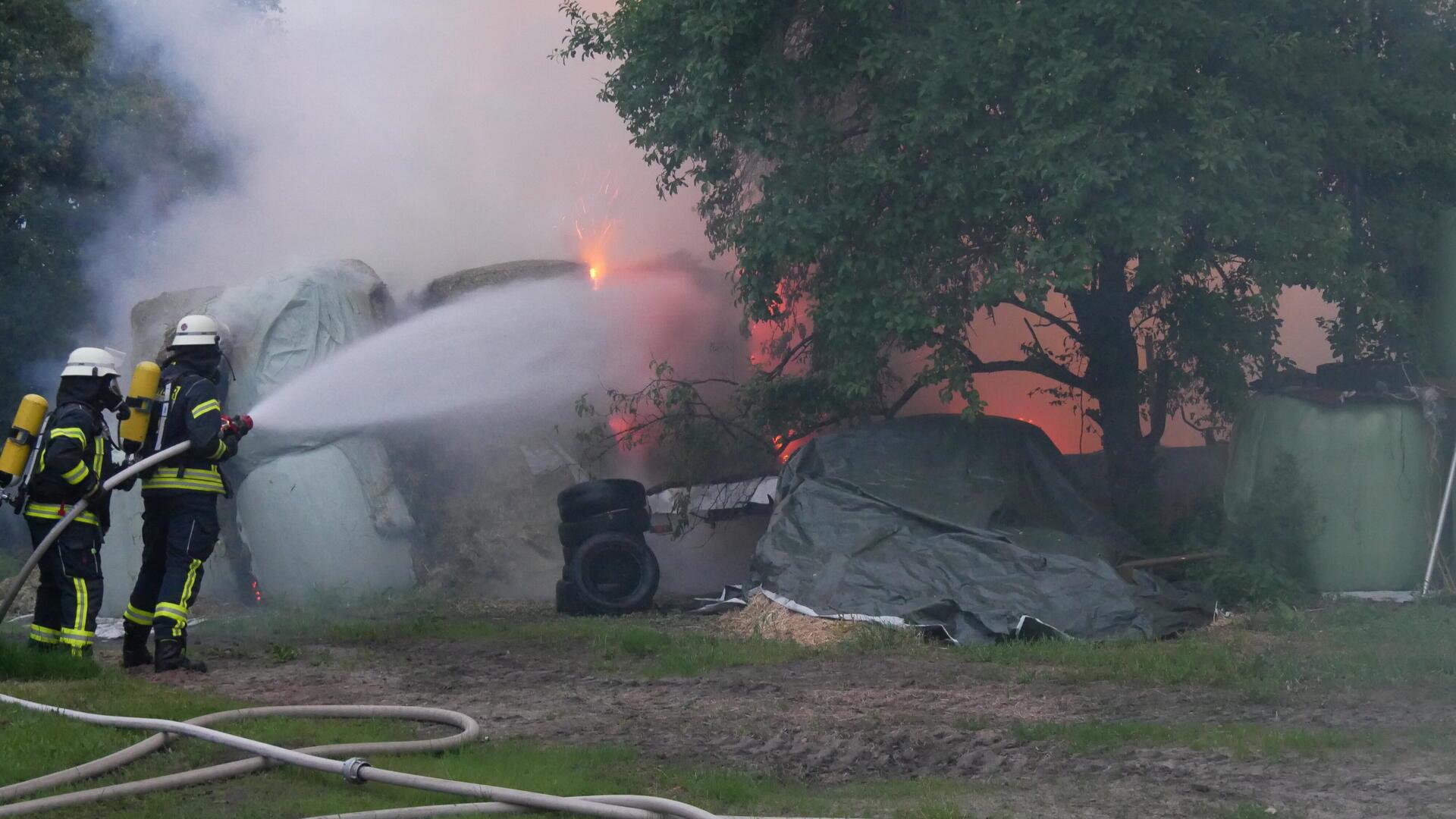 Feuerwehrleute halten einen Schlauch und richten den Wasserstrahl auf Flammen. 
