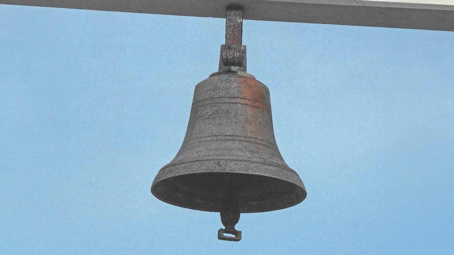Man sieht eine alte Messingglocke vor blauem Hintergrund.