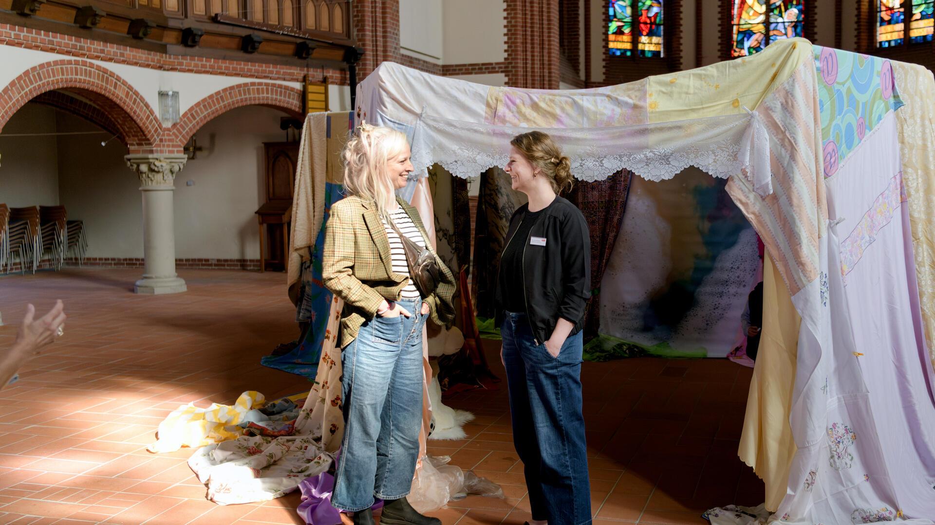 Die Hamburger Künstlerin Jenny Schäfer (links) und Dr. Lena Reichelt, Leiterin der Kulturkirche Bremerhaven, laden in „Innere Oberflächen“ in der Pauluskirche ein. Dazu, durch die Stoff-Höhle zu flanieren und sich an Kindertage der Geborgenheit, an die innere Heimat, zu erinnern. Foto: Masorat - f
