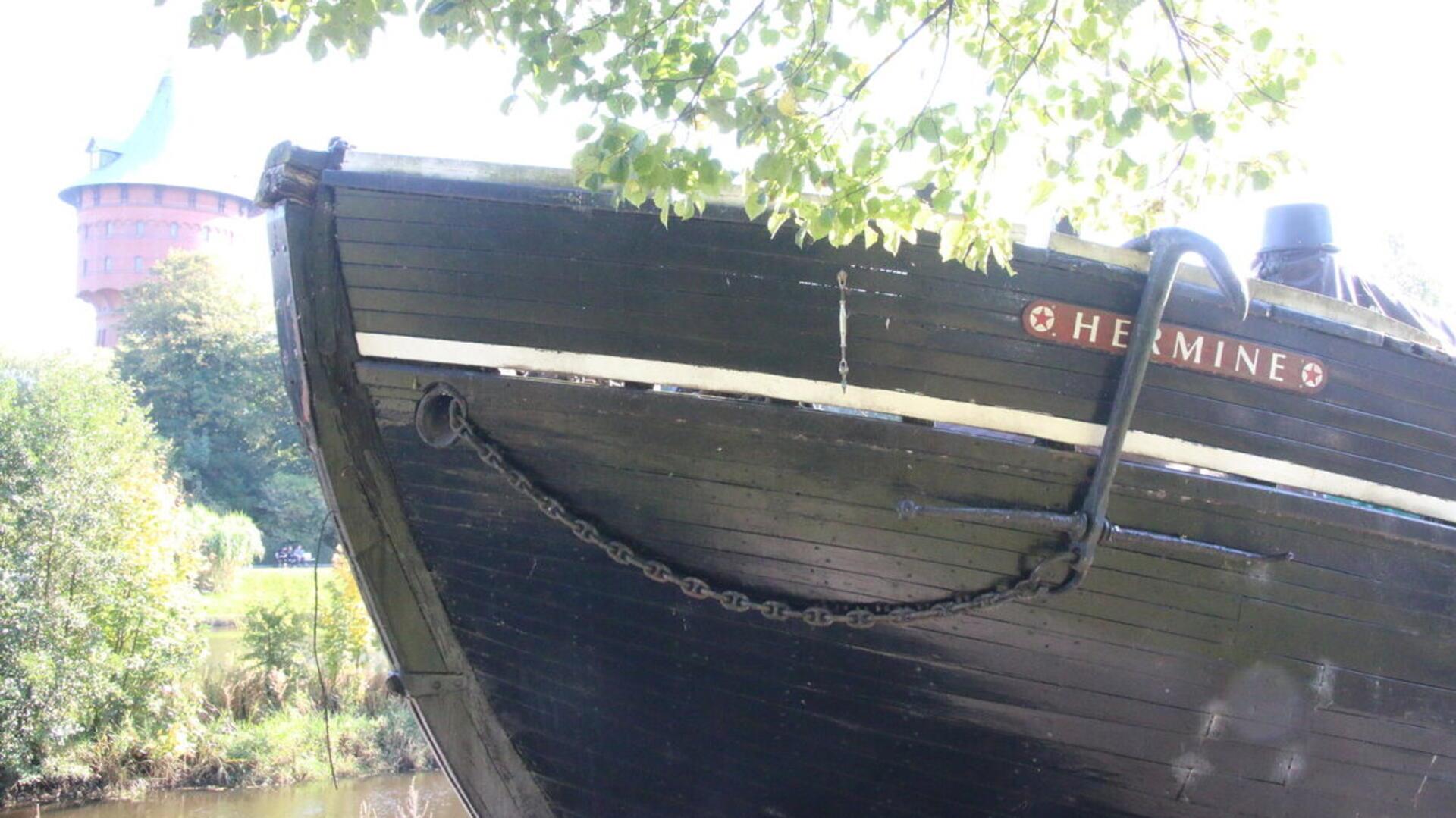 Die „Hermine“ liegt im Sonnenlicht am Schleusenpriel und verfällt zusehends – das marode Holzschiff ist längst kein Aushängeschild der Stadt mehr, sondern ein Sinnbild kommunaler Vernachlässigung.