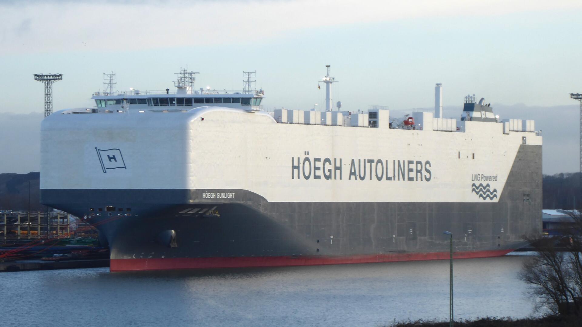 Ein großes Autotransportschiff der Reederei Höegh Autoliners mit dem Namen „Höegh Sunlight“ in einem Hafen. Das Schiff ist weiß und grau lackiert und trägt die Aufschrift „LNG Powered“.