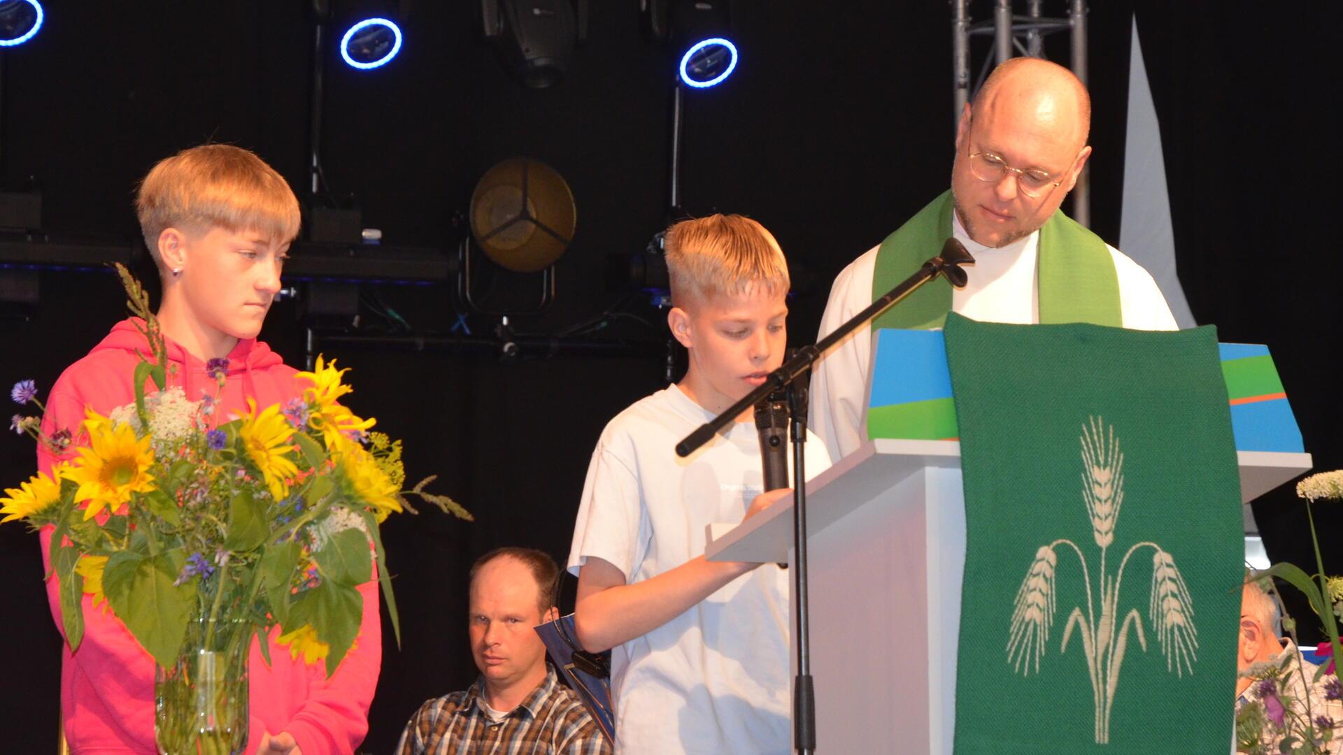 Zwei Jungen mit einem Pastor auf der Bühne.