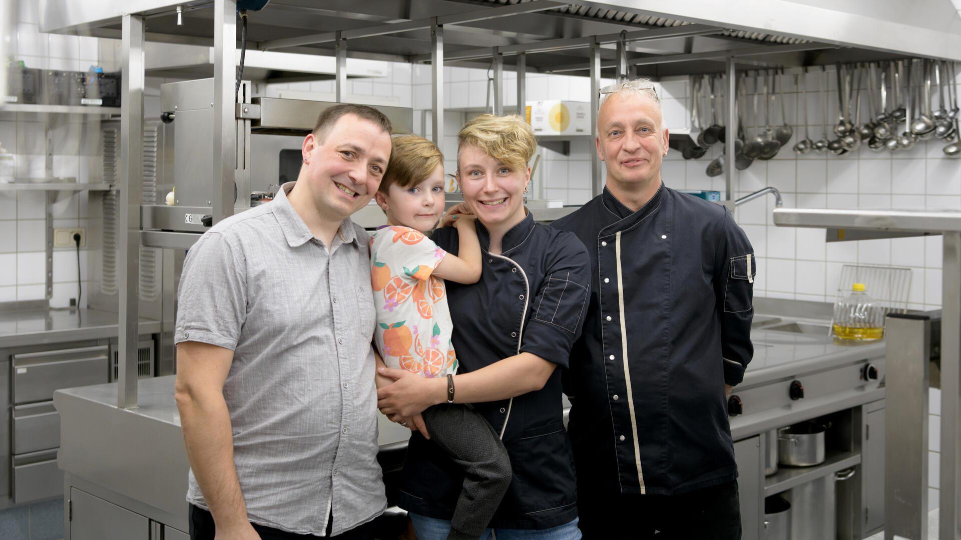 Familie mit zwei Männern, eine Frau mit Kind auf dem Arm in einer Restaurant-Küche